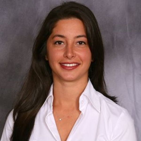 Woman with long dark hair smiling in white shirt.