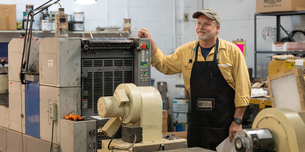 A company employee operates the offset printing machine to make custom paper products.