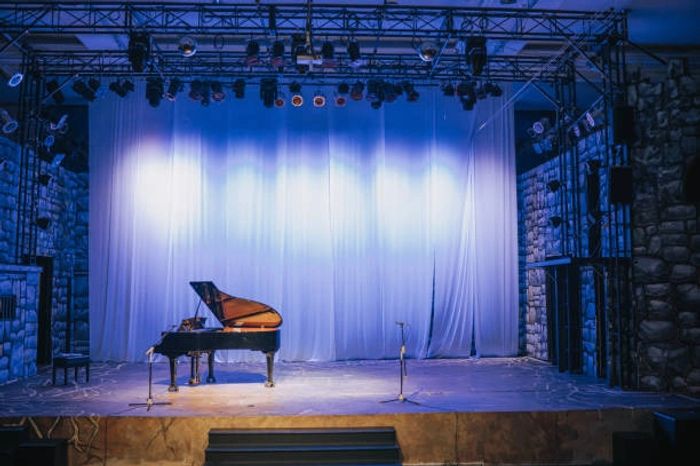 Empty stage with grand piano under blue lighting and microphones.
