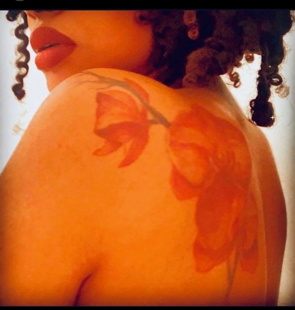 Close-up of a woman with curly hair and a red flower tattoo on her shoulder.