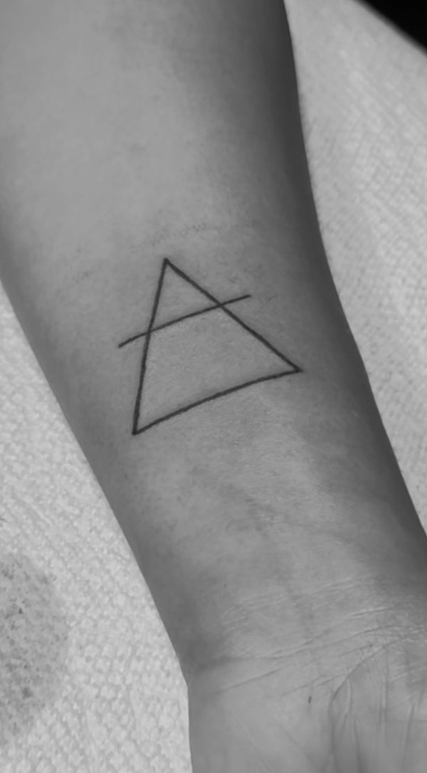 Minimalistic tattoo of an outlined triangle crossed by a single line on a wrist.