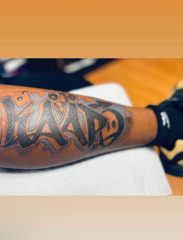 Bold black and gray graffiti-style tattoo on forearm.