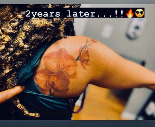 Close-up of a faded flower tattoo on a shoulder with text saying '2 years later...!'