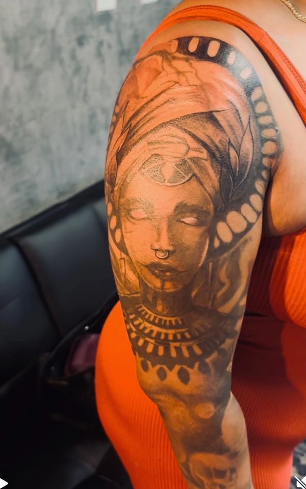 Tattoo of a mystical woman with a third eye and tribal patterns on the upper arm.