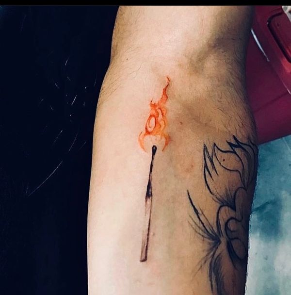 Tattoo of a lit match with orange flame on the arm.