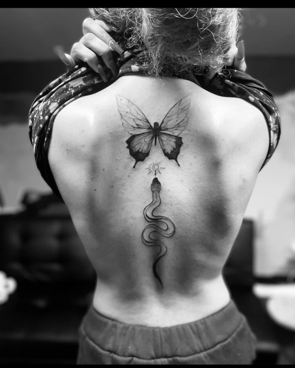 Black and white tattoo of a butterfly and snake on a person's back.