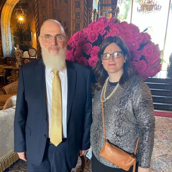 Two people standing with flowers in the back.