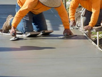Workers smoothing freshly poured concrete on a sidewalk.