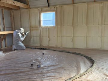 Person spray painting insulation inside a room.