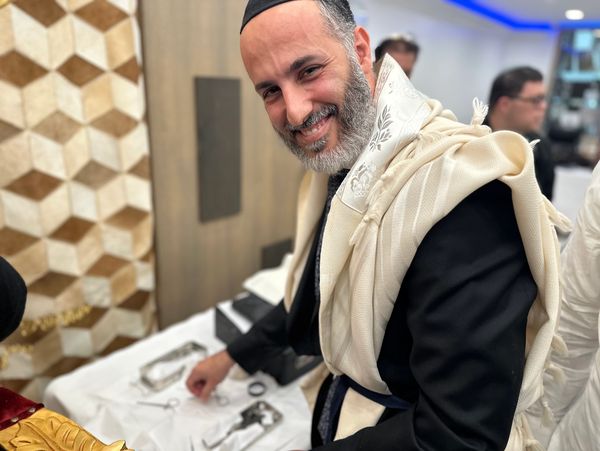 A joyful man dressed in traditional Jewish attire smiles warmly.