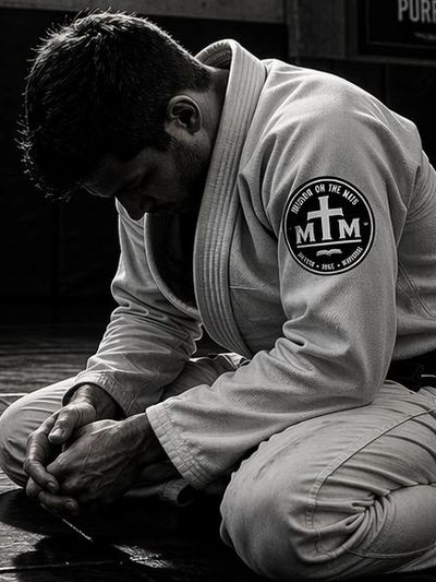 Man in martial arts gi kneeling with head bowed, deep in thought or prayer.