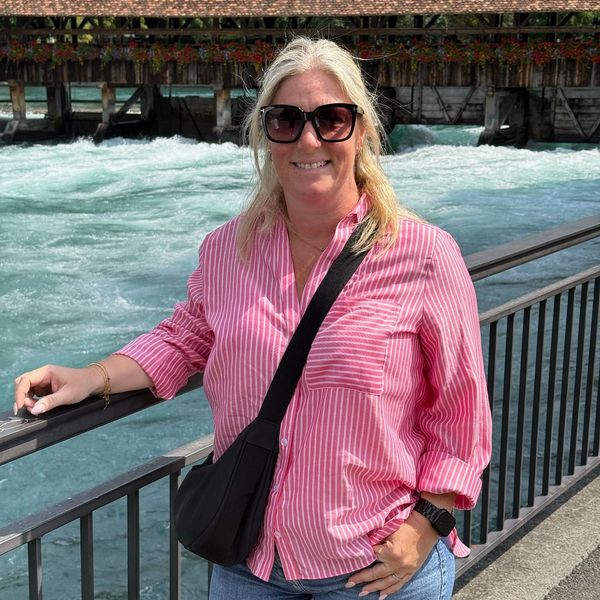 Katy Smith wearing a pink striped shirt standing by a river 