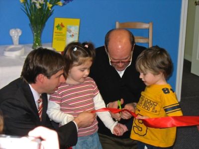 Children and adults cutting a ribbon at an event.