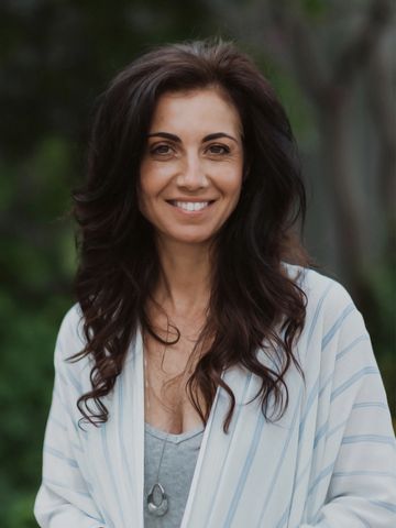 Smiling woman with long wavy hair outdoors in casual attire.
