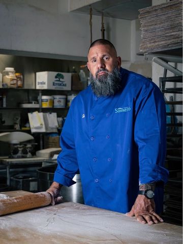 Chef in a blue uniform stands confidently in a bakery kitchen.