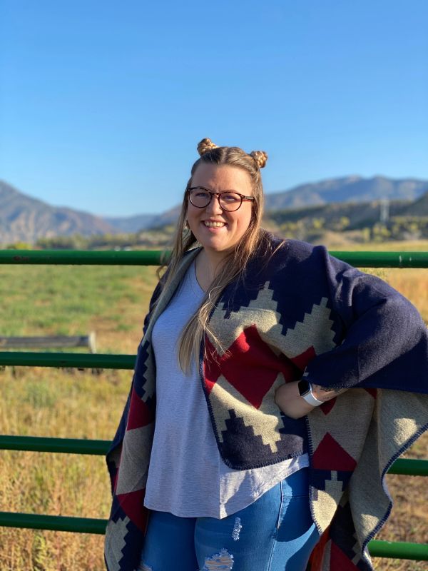 Smiling woman outdoors wearing glasses and a patterned shawl.