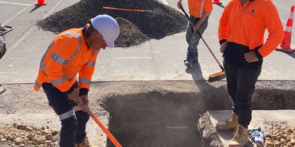 Workers in orange safety gear digging a large hole on a construction site.