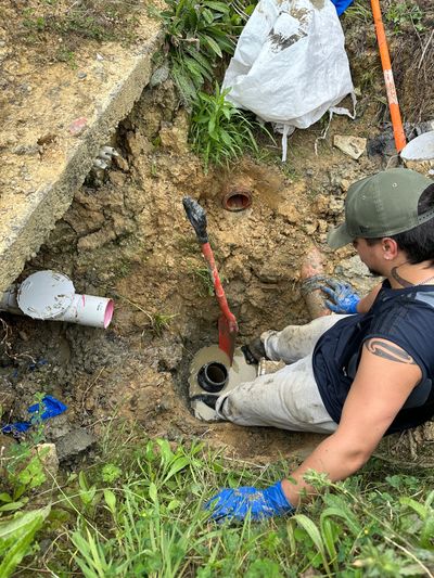 Person working on an underground pipe in a muddy hole.