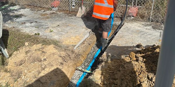 Worker in orange vest installing blue pipe in trench at construction site.
