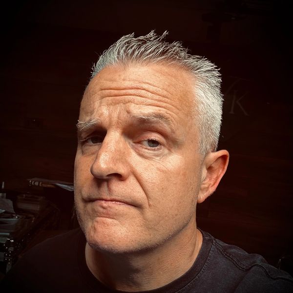 Close-up of a middle-aged man with gray hair and a skeptical expression.