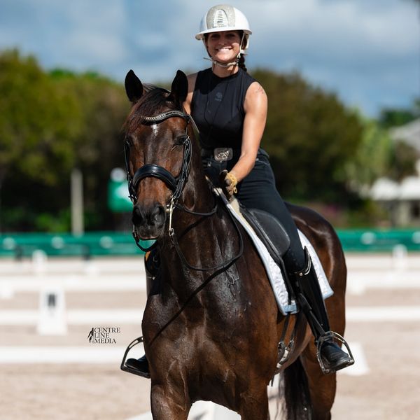 Smiling rider on a dark brown horse at an outdoor arena.