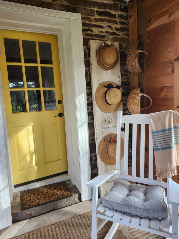 Cozy porch with yellow door, hats, and rocking chair.