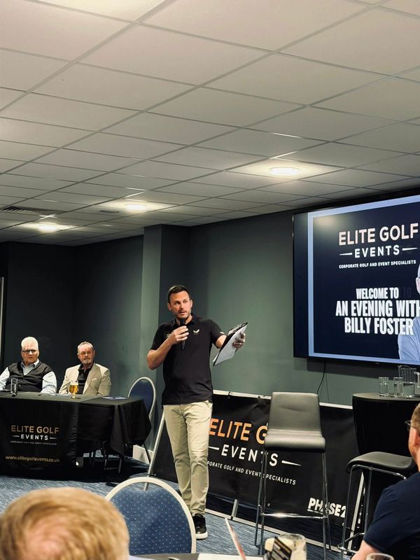 A man speaking at a golf event with an audience seated.