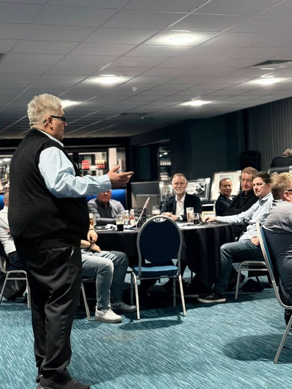 Man speaking to a group seated around tables in a conference room.