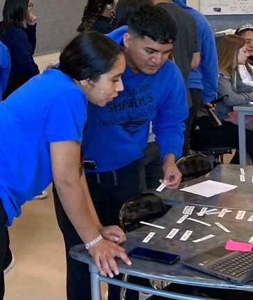 Two students collaborate over word strips on a classroom table.