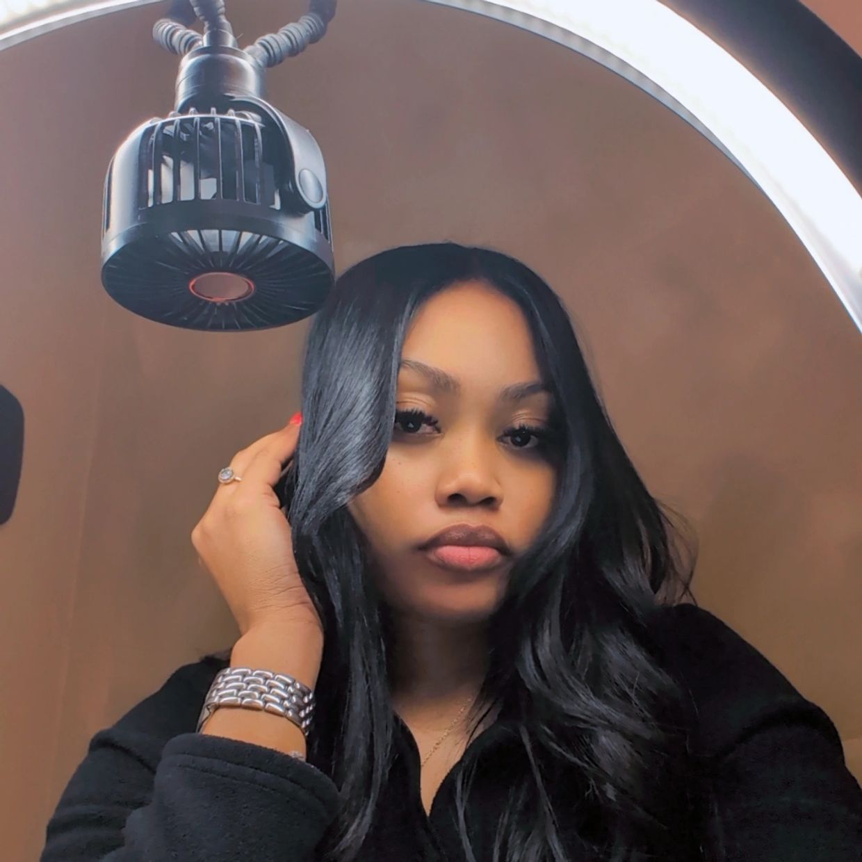 Woman with long black hair under a circular LED light ring.