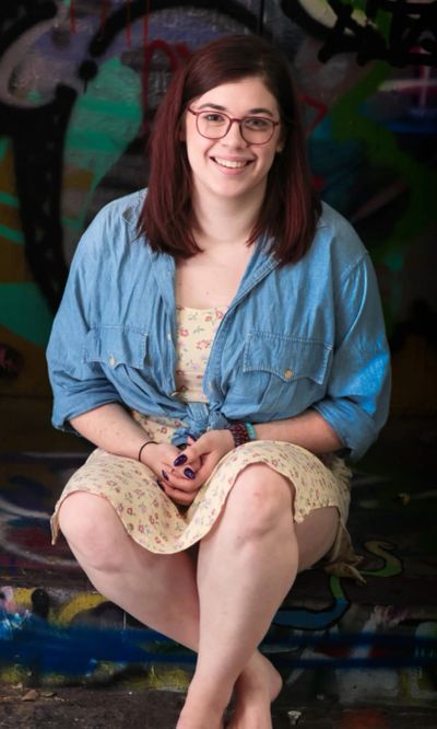 Smiling woman with glasses sitting against a graffiti wall.