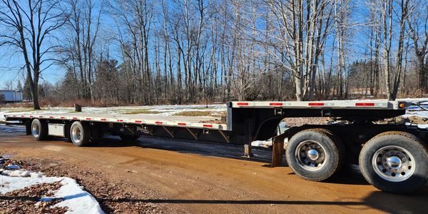 Flatbed trailer parked on a dirt road in a snowy, wooded area.