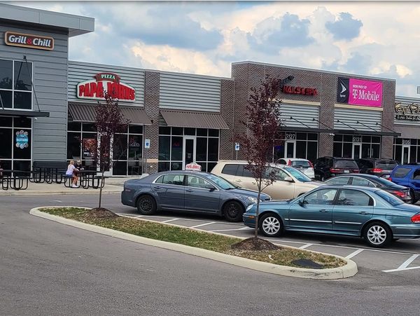 Shopping center parking lot with various stores and cars.
