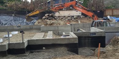 Construction site with concrete foundation and excavator in the background.