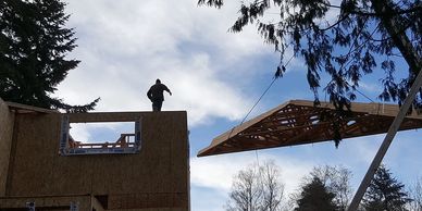 Construction worker guiding a roof truss into place on a building frame.