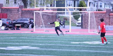 Soccer goalie in yellow prepares to stop a penalty kick on a green field.