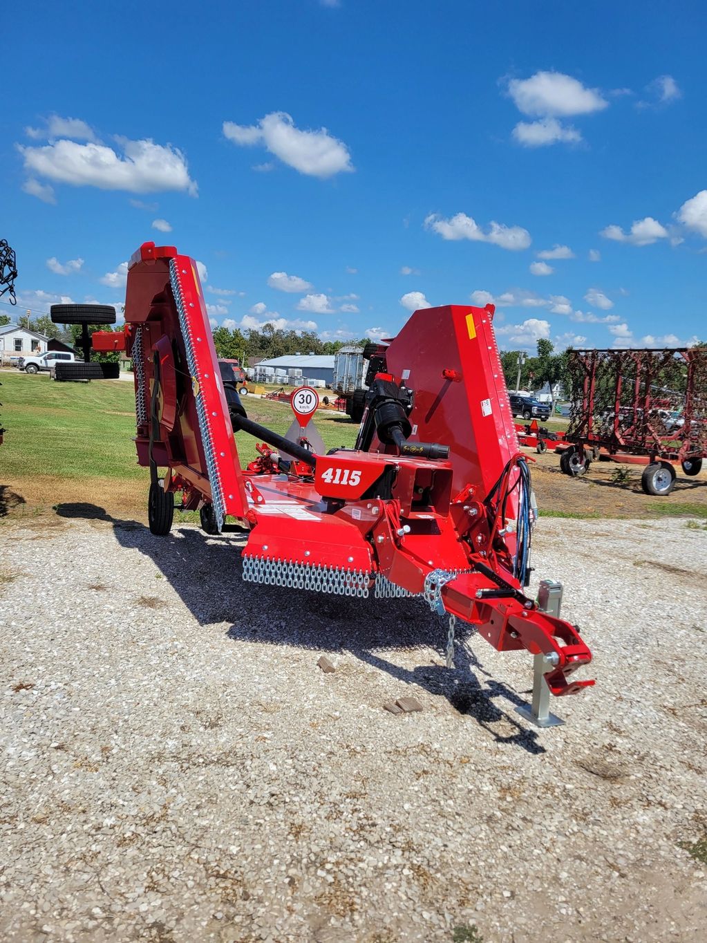 Red agricultural machinery under a bright blue sky on a gravel lot.