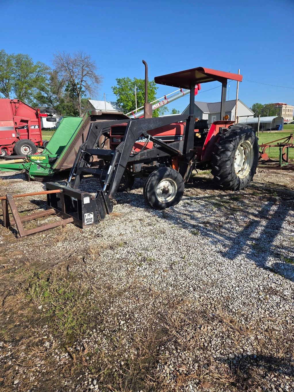 Red tractor with front loader attachment parked on gravel.