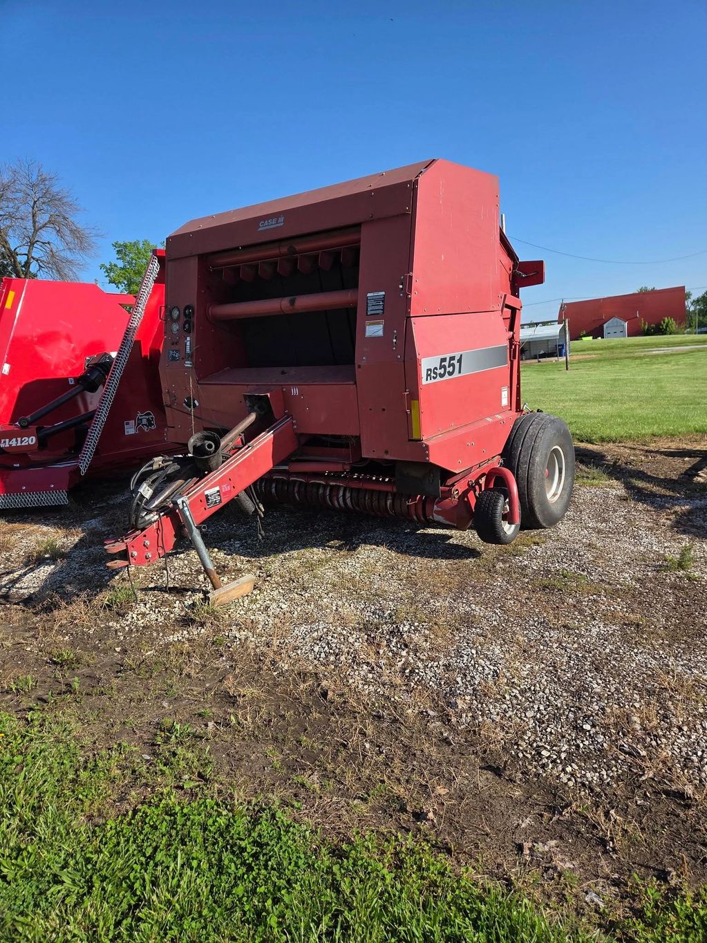 Red RS551 Case IH round baler parked on gravel under clear blue sky.