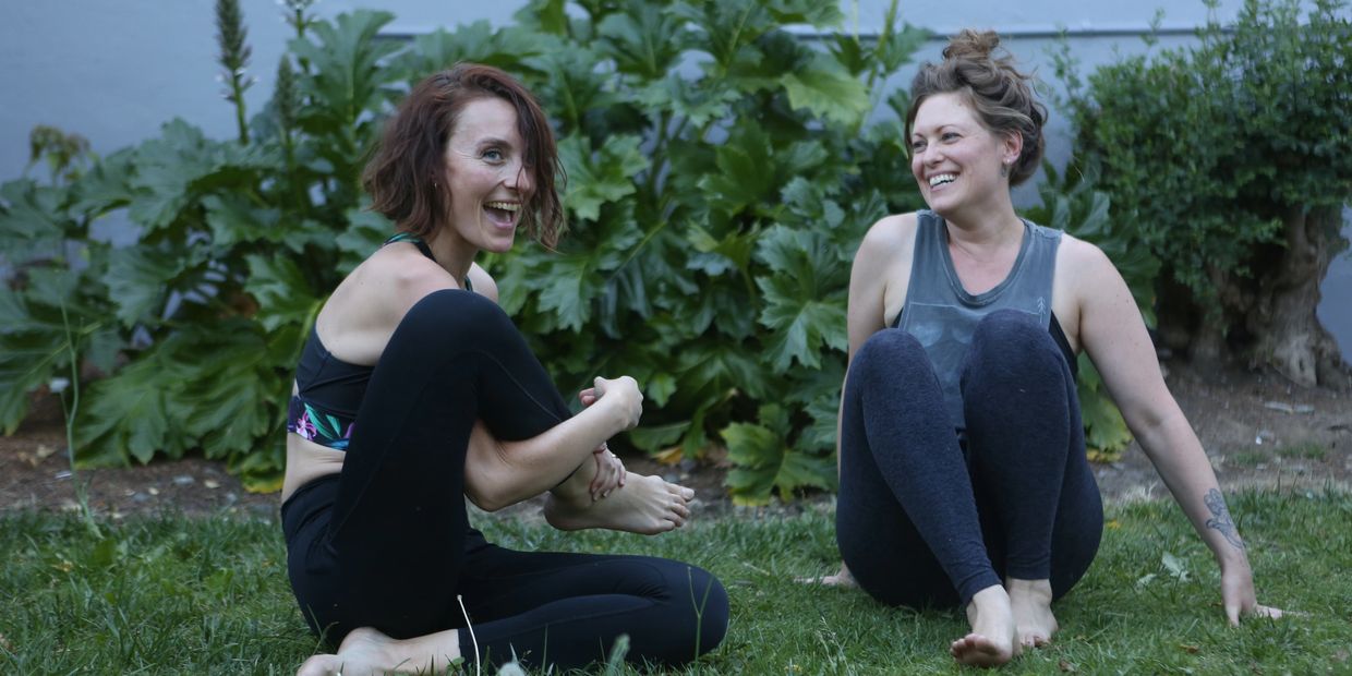 Lisa and Natacha laughing as they fall out of a yoga pose