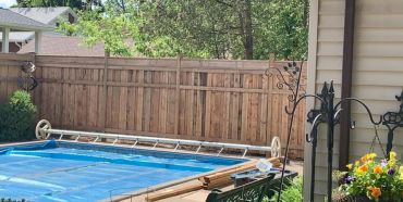 Backyard pool covered with a blue tarp and surrounded by a wooden fence.