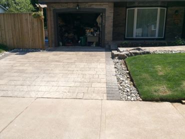 Newly paved driveway with stone border and adjacent green lawn.