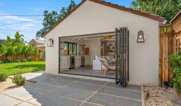 Open-concept outdoor kitchen and lounge area with bi-fold doors and garden view.