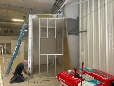 Worker assembling metal framing for interior wall in construction site.