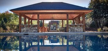 A poolside pavilion with stone walls and wooden beams reflected in the water.