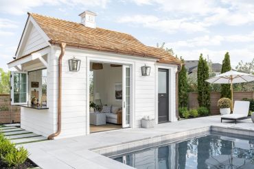 Modern pool house with open doors and a cozy outdoor seating area.