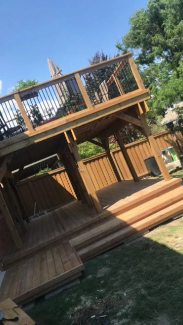 A two-level wooden deck with stairs and railings in a backyard.