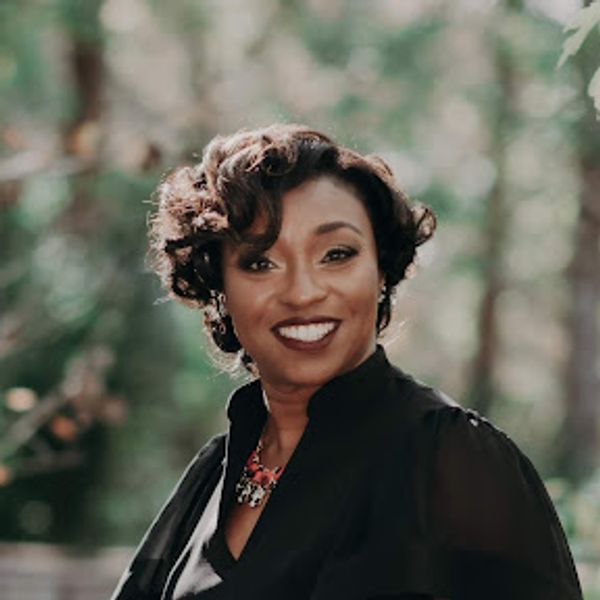 Smiling woman with curly hair in black outfit outdoors.