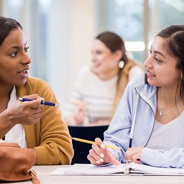Two women engaged in a focused study discussion in a classroom.