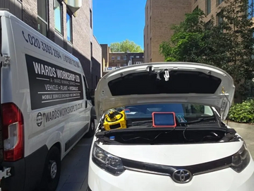 A white car with its hood open being serviced next to a Wards Workshop van.